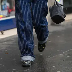 Person mit gestreiften Hosen, die die Jeans umschlagen. Schwarze Schuhe mit Sternenapplikationen und eine kleine Tasche.