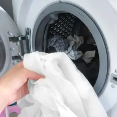 Hand lädt weiße Wäsche in die Waschmaschine. Zeit, die neuen Hemden zu waschen und sie frisch zu machen.