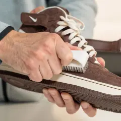 Hände pflegen braune Lederschuhe mit einer Bürste.