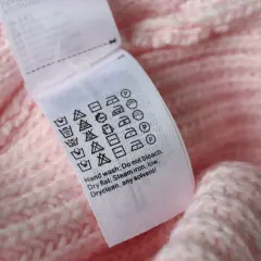 Pflegeetikett auf rosa Strickware: Waschsymbol 30 Grad mit 2 Strichen zeigt schonende Maschinenwäsche.