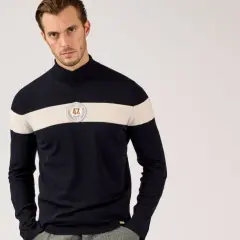 Mann in dunkelblauem Rollkragenpullover mit breitem cremefarbenem Streifen und Emblem. So kann man Rollkragenpullover kombinieren, Herren-Style.