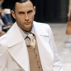 Ein Mann auf dem Laufsteg trägt einen weißen Trenchcoat über einem beigen Sakko, das er elegant kombiniert.