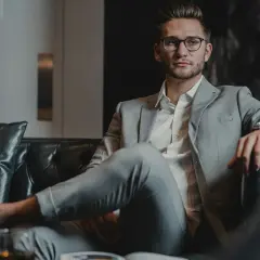 Junger Mann in stilvoller Business-Kleidung für Herren, entspannt auf einem Ledersofa mit einem Glas Whiskey.