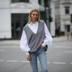 Eine Frau in einem weißen Hemd und Jeans trägt einen grauen Strick-Pullunder. So kann man Pullunder Damen kombinieren für einen lässigen Look.
