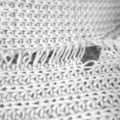 Nahaufnahme eines verfilzten und eingelaufenen Pullovers. Die Strickstruktur ist sichtbar, mit ausgefransten Fäden und einem Loch.
