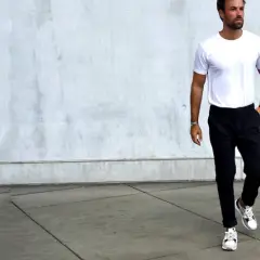 Mann in weißem T-Shirt und schwarzer Chino-Hose, dazu weiße Sneaker. Ein Beispiel, welche Schuhe zur Chino Hose Herren passen.