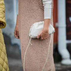 Ein gelber Steppmantel und ein Strickkleid mit weißem Langarmshirt darunter – ein perfekter layering look. Eine weiße Clutch rundet das Outfit ab.