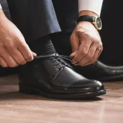Mann schnürt schwarze Anzugschuhe. Die Wahl der richtigen Socken zum Anzug ist entscheidend für einen perfekten Look.