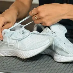 Hände binden Schnürsenkel an hellblauen Mesh-Schuhen, bereit für die Reinigung.