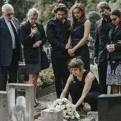 Trauernde Familie in schwarzer Kleidung, was zieht man zur Beerdigung an? Eine Frau legt Blumen nieder.