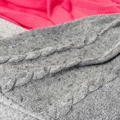 Grauer Strickpullover mit Zopfmuster, auf dem sich deutliches Pilling zeigt. Dies ist ein häufiger Reklamationsgrund bei Wollpullovern.