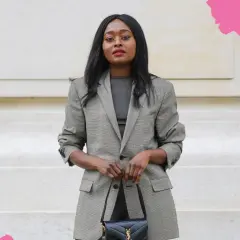 Eine Frau in einem karierten Blazer und dunklem Oberteil verkörpert smart business casual. Sie trägt eine schwarze Handtasche.