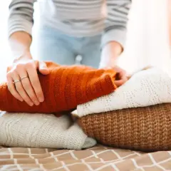 Hände falten einen Stapel warmer Strickpullover. Der orangefarbene Pullover liegt oben. Das Waschen von Wollpullovern erfordert Sorgfalt.