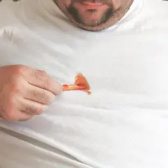 Mann mit fettigen Pommes auf weißem T-Shirt. Tipps, wie man fettflecken aus kleidung entfernen nach dem waschen kann.