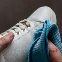 Hände polieren weiße Sneaker mit einem blauen Tuch. So werden die schuhe sauber machen und sehen wieder wie neu aus.