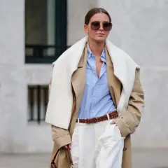 Eine Frau trägt einen beigefarbenen Trenchcoat, ein hellblaues Hemd und weiße Hose. Das Outfit zeigt, wie man ein beiges Oberteil kombinieren kann, auch für Herren.