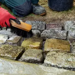 Mit roter Handschuh und Bürste werden eingetrocknete Fettflecken von Natursteinen entfernt.