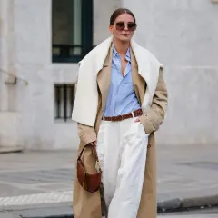 Frau im Trenchcoat, hellblauem Hemd und weißen Hosen, ein perfekter casual business look. Braune Tasche und Gürtel.