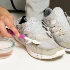 Schuhe reinigen: Mit einer Bürste und Seifenwasser werden Grasflecken von grauen Sneakern entfernt.