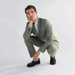 Mann in grauem Anzug und schwarzen Loafern zum Anzug, der nachdenklich auf einem Knie sitzt.