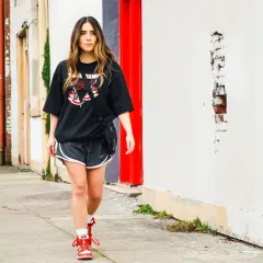 Frau stylt ein oversized T-Shirt mit Shorts und Sneakern, geht auf einem Bürgersteig.