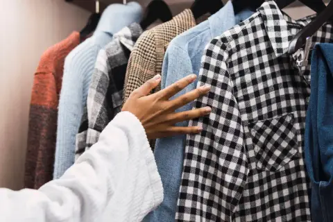 Hand streicht über Kleidung im Schrank. So kann man muffigen Geruch aus Kleidung entfernen.