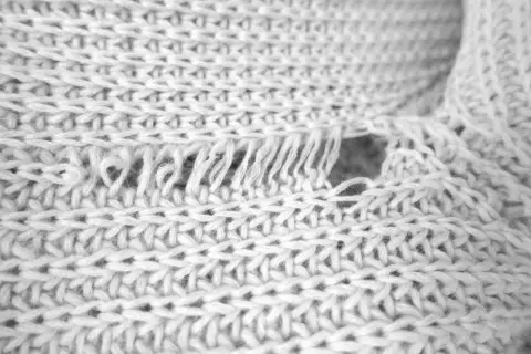Nahaufnahme eines verfilzten und eingelaufenen Pullovers. Die Strickstruktur ist sichtbar, mit ausgefransten Fäden und einem Loch.