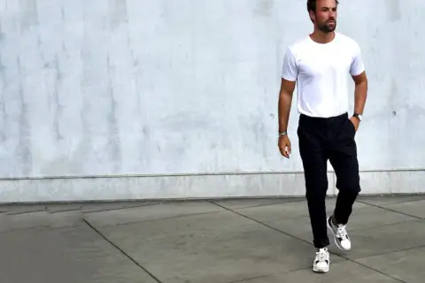 Mann in weißem T-Shirt und schwarzer Chino-Hose, dazu weiße Sneaker. Ein Beispiel, welche Schuhe zur Chino Hose Herren passen.