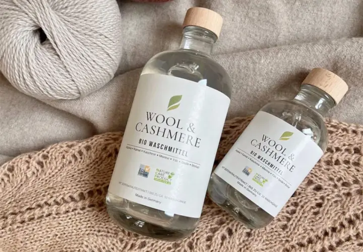Zwei Flaschen "Wool & Cashmere" Bio-Waschmittel neben Garnknäueln und Strickwaren. Perfekt für die sanfte **Wolle waschen mit Shampoo**.