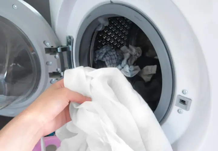 Hand lädt weiße Wäsche in die Waschmaschine. Zeit, die neuen Hemden zu waschen und sie frisch zu machen.