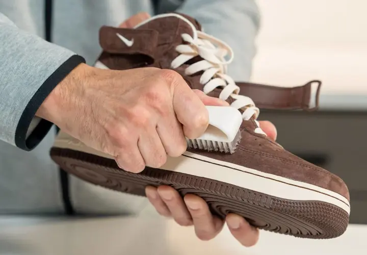 Hände pflegen braune Lederschuhe mit einer Bürste.