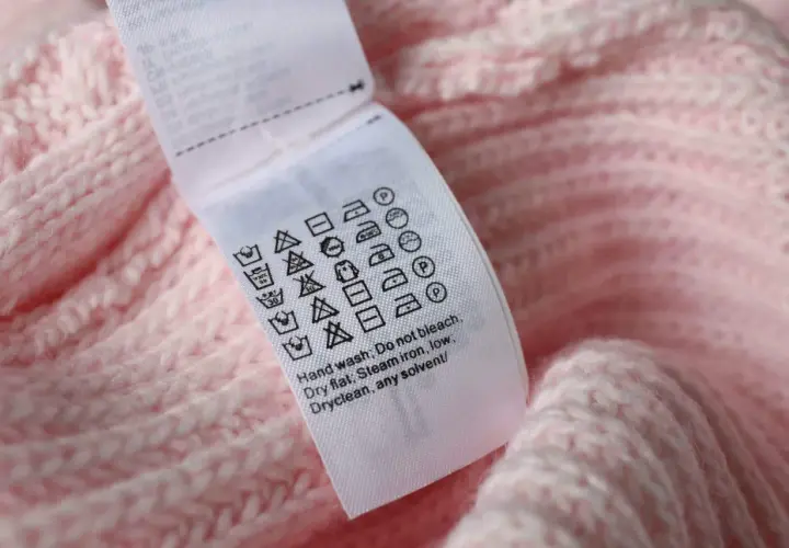 Pflegeetikett auf rosa Strickware: Waschsymbol 30 Grad mit 2 Strichen zeigt schonende Maschinenwäsche.