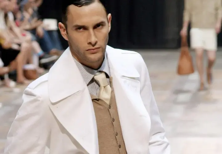 Ein Mann auf dem Laufsteg trägt einen weißen Trenchcoat über einem beigen Sakko, das er elegant kombiniert.