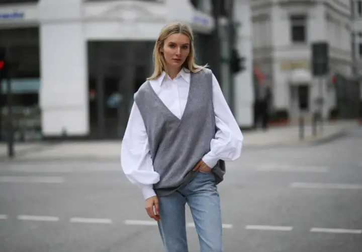 Eine Frau in einem weißen Hemd und Jeans trägt einen grauen Strick-Pullunder. So kann man Pullunder Damen kombinieren für einen lässigen Look.