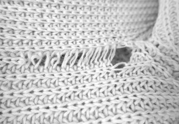 Nahaufnahme eines verfilzten und eingelaufenen Pullovers. Die Strickstruktur ist sichtbar, mit ausgefransten Fäden und einem Loch.