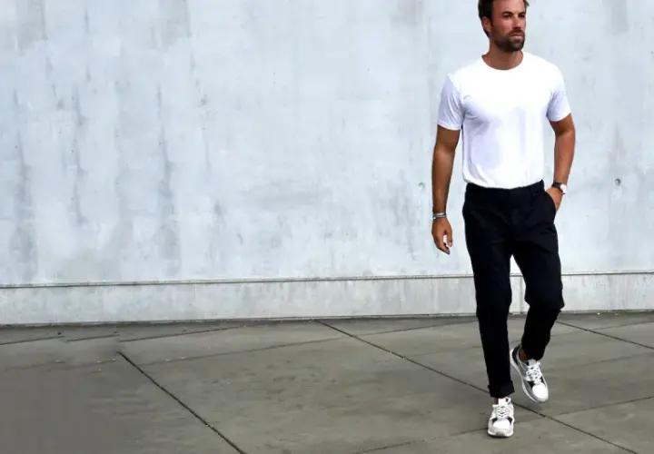 Mann in weißem T-Shirt und schwarzer Chino-Hose, dazu weiße Sneaker. Ein Beispiel, welche Schuhe zur Chino Hose Herren passen.