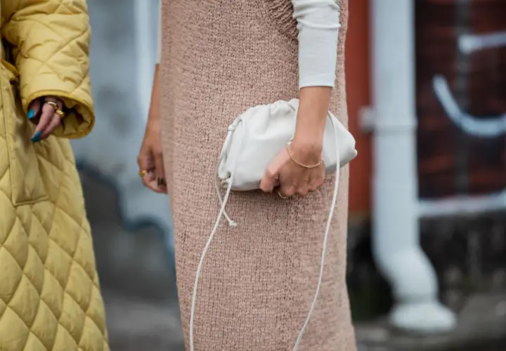 Ein gelber Steppmantel und ein Strickkleid mit weißem Langarmshirt darunter – ein perfekter layering look. Eine weiße Clutch rundet das Outfit ab.