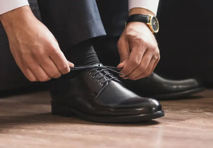 Mann schnürt schwarze Anzugschuhe. Die Wahl der richtigen Socken zum Anzug ist entscheidend für einen perfekten Look.