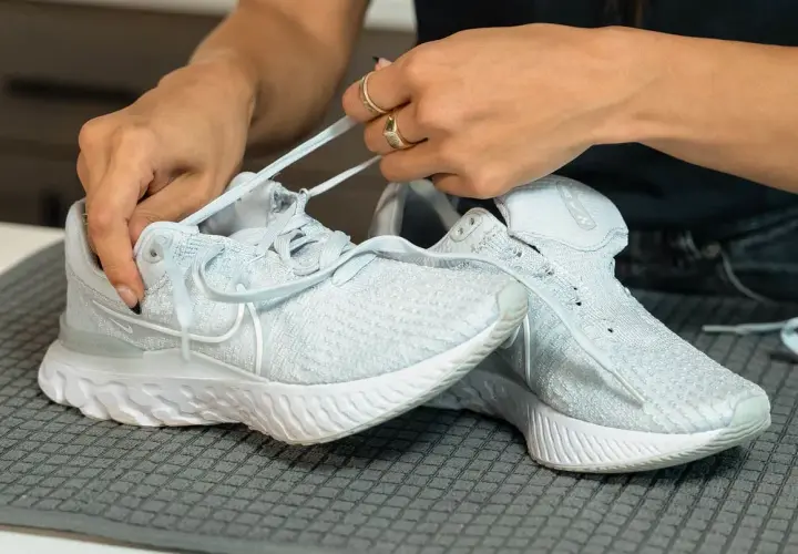 Hände binden Schnürsenkel an hellblauen Mesh-Schuhen, bereit für die Reinigung.
