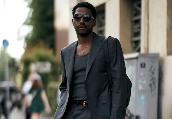 Ein Mann trägt einen eleganten Anzug mit Sneaker, dazu eine Kette und Sonnenbrille.
