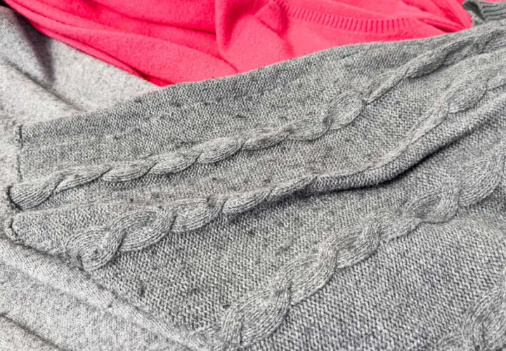 Grauer Strickpullover mit Zopfmuster, auf dem sich deutliches Pilling zeigt. Dies ist ein häufiger Reklamationsgrund bei Wollpullovern.