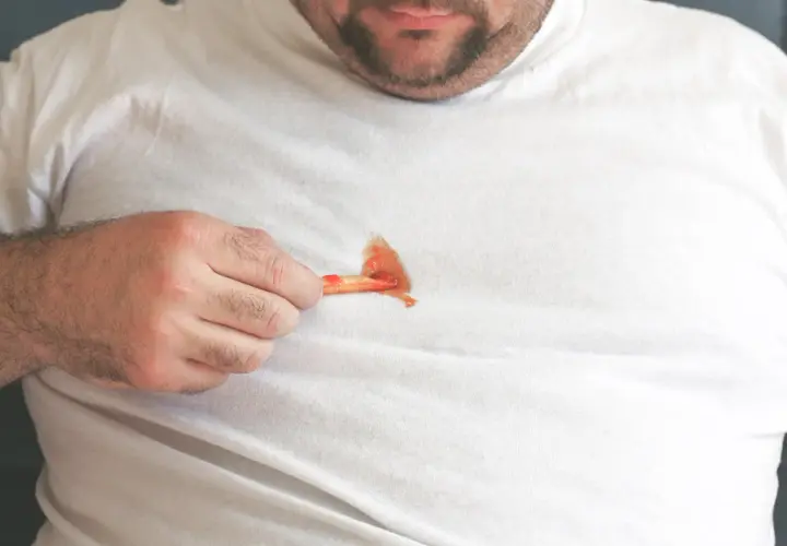 Mann mit fettigen Pommes auf weißem T-Shirt. Tipps, wie man fettflecken aus kleidung entfernen nach dem waschen kann.