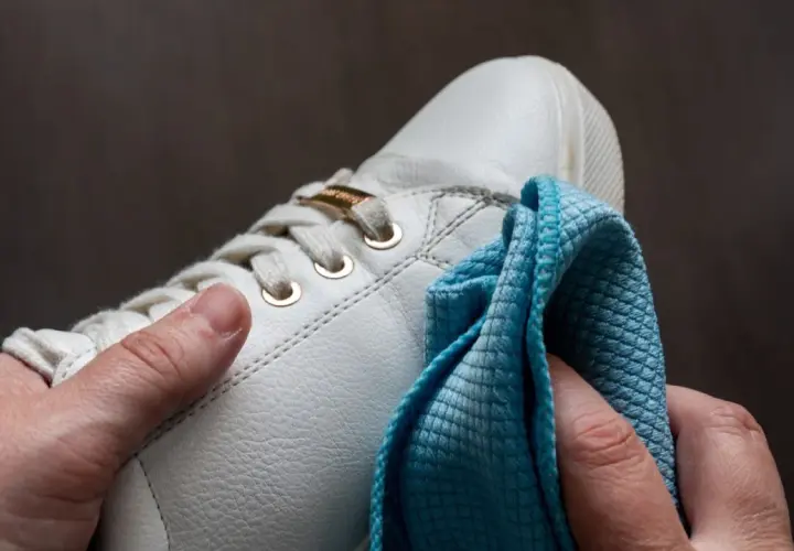 Hände polieren weiße Sneaker mit einem blauen Tuch. So werden die schuhe sauber machen und sehen wieder wie neu aus.