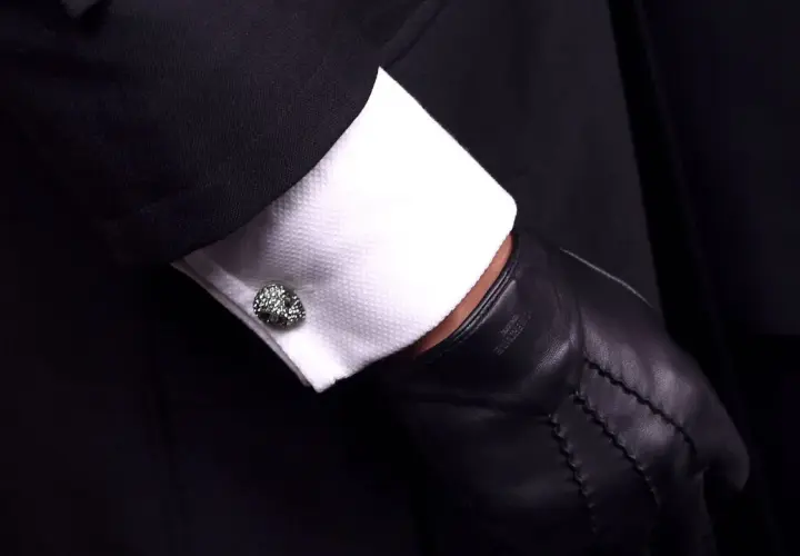 Elegante Manschettenknöpfe zieren das weiße Hemd unter einem schwarzen Anzug. Sie sind kleine Schmuckstücke, die zeigen, was sind Manschetten.