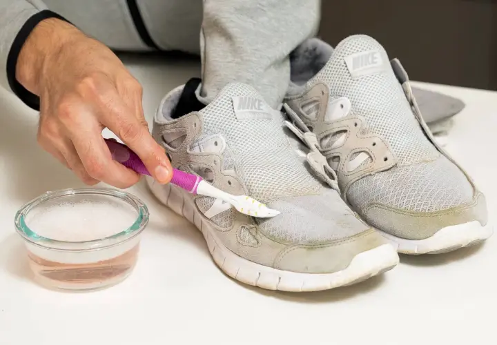 Schuhe reinigen: Mit einer Bürste und Seifenwasser werden Grasflecken von grauen Sneakern entfernt.