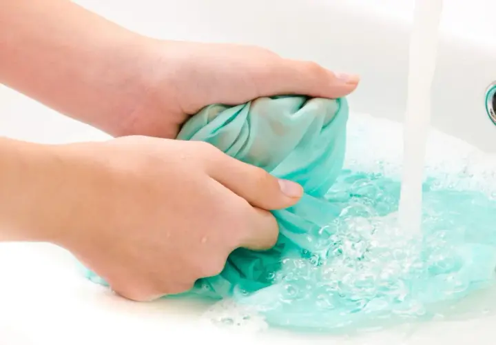Hände waschen ein türkises Tuch in der Spüle, um Fettspritzer zu entfernen.