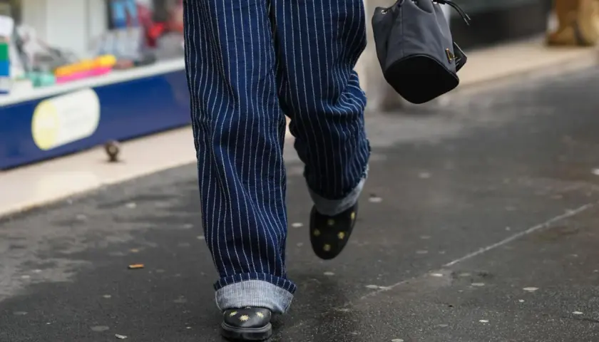 Person mit gestreiften Hosen, die die Jeans umschlagen. Schwarze Schuhe mit Sternenapplikationen und eine kleine Tasche.