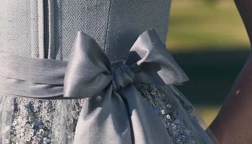 Ein Dirndl mit einer großen, grauen Schleife. Die Schleife ist Teil des Kleides, das auch mit Pailletten und Stickereien verziert ist. Perfekt für Kinder, die sich festlich kleiden möchten.