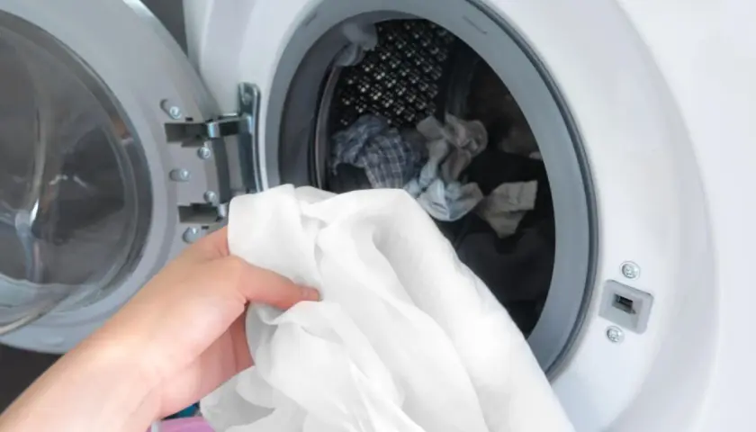 Hand lädt weiße Wäsche in die Waschmaschine. Zeit, die neuen Hemden zu waschen und sie frisch zu machen.
