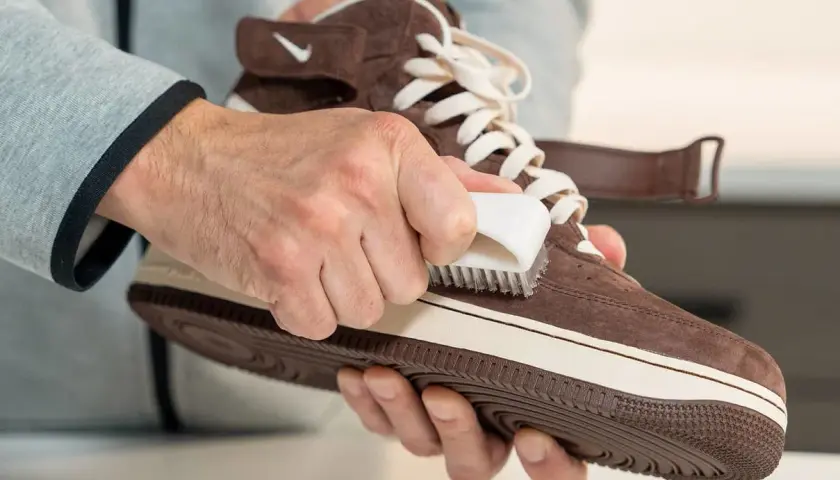 Hände pflegen braune Lederschuhe mit einer Bürste.
